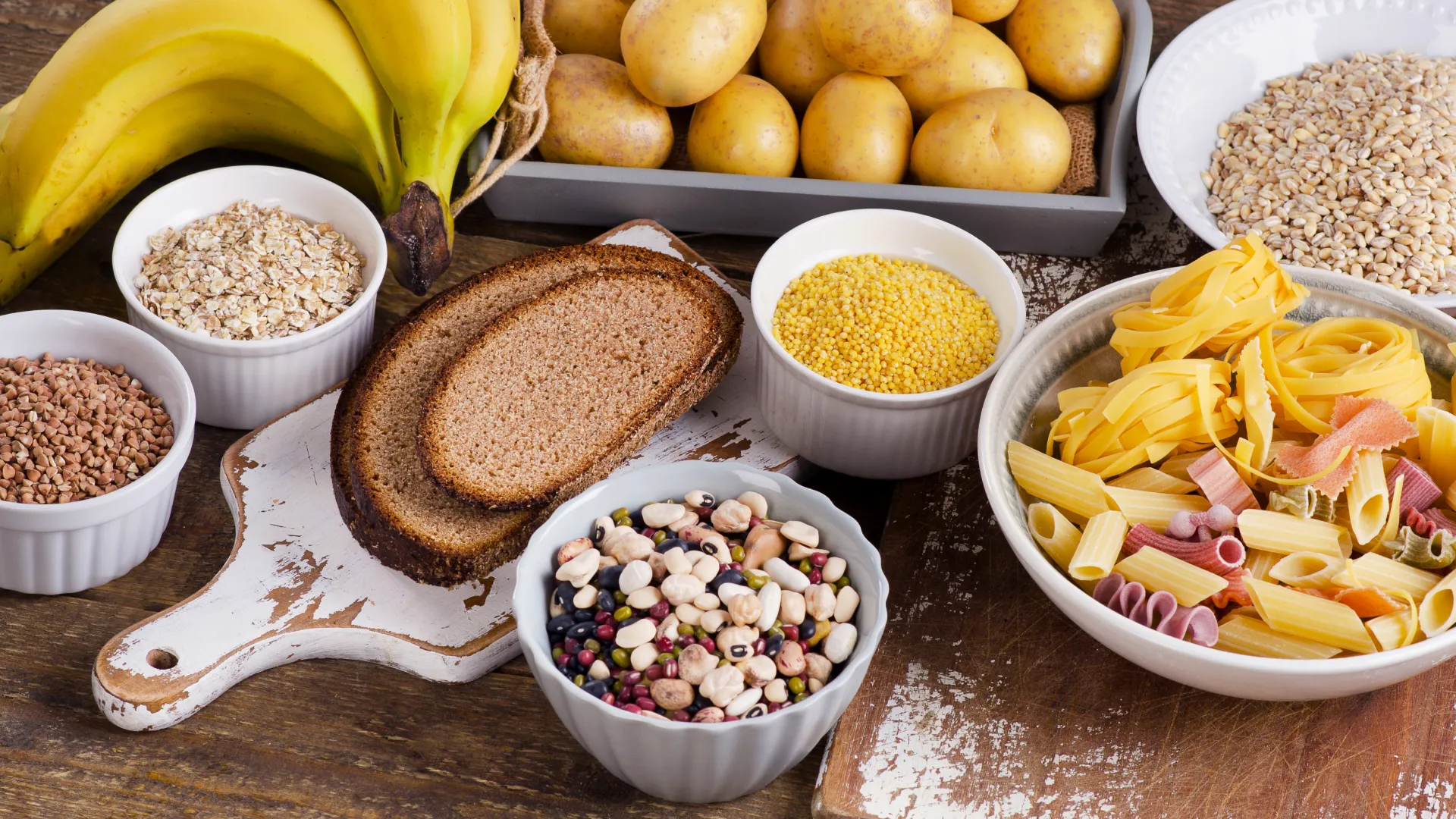 Ein Teller mit verschiedenen kohlenhydratreichen Lebensmitteln, darunter Brot, Nudeln, Reis, Kartoffeln und Haferflocken.